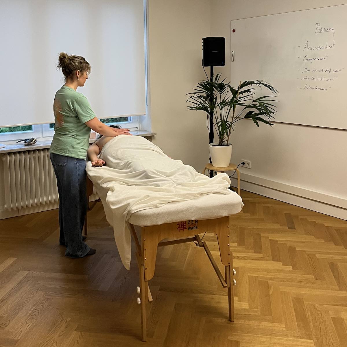 Eine Teilnehmerin des Kurses für Psychic Massage massiert eine andere Teilnehmerin während einer Partnerübung. Im Hintergrund ein Whiteboard mit Informationen.