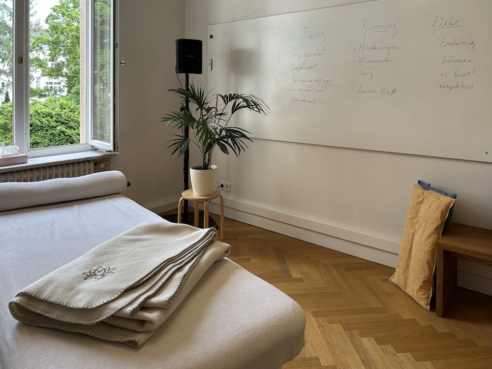 Kursraum mit Therapieliege im Vordergrund und Whiteboard mit Kursinhalten im Hintergrund